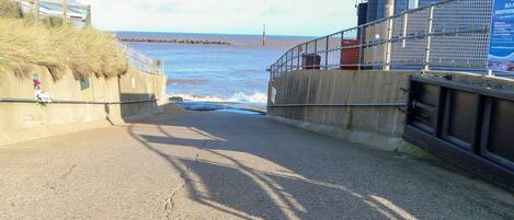 A coastal road leading to the sea with a concrete barrier on one side and a metal railing on the other.
