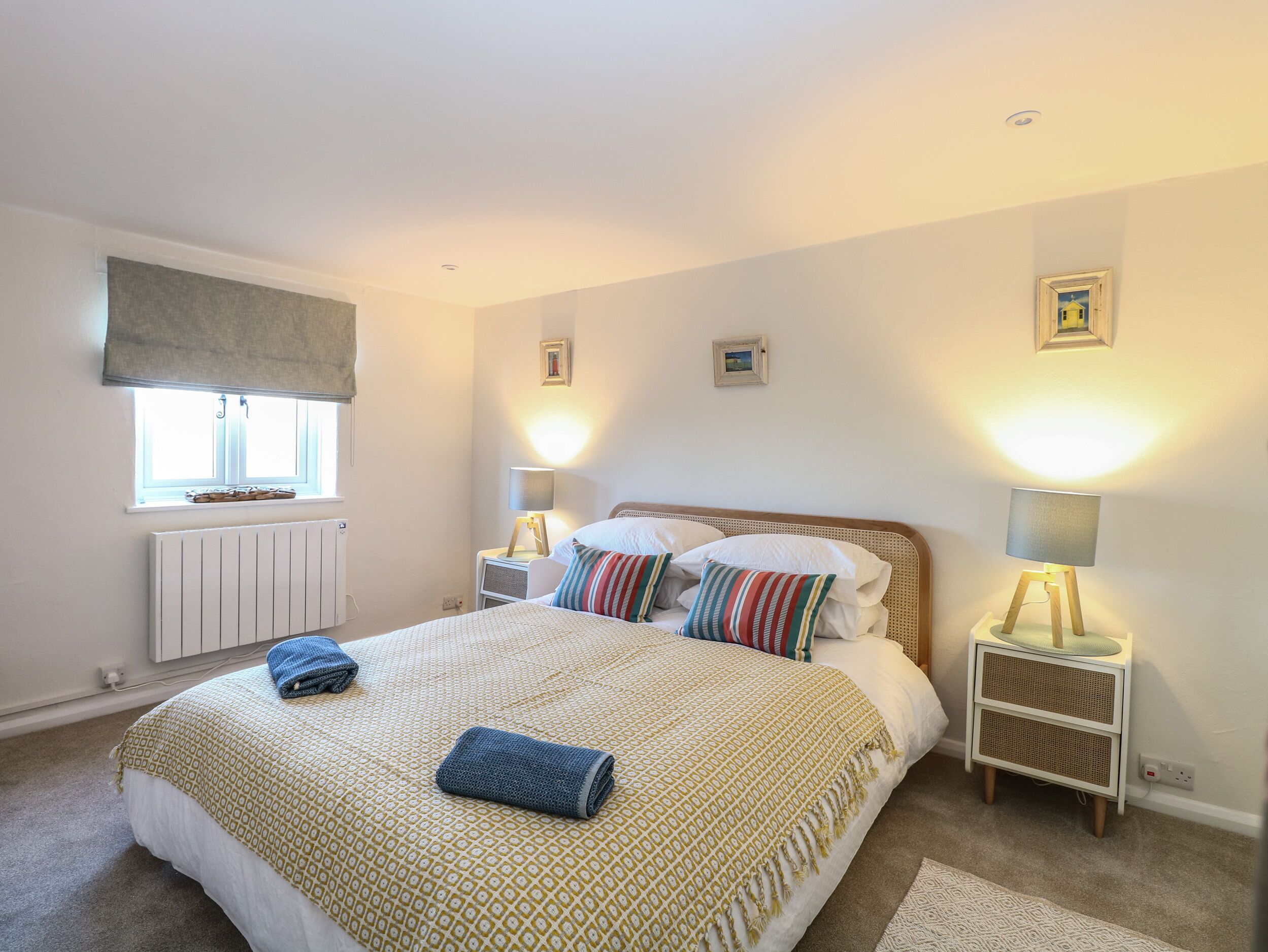 A bedroom with a bed, bedside lamps, a window with a view, a radiator, and a small table with a lamp.