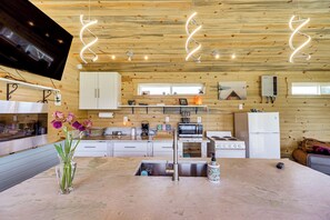 A modern kitchen with wooden walls, a central island, stainless steel appliances, and a flat-screen TV. - Skydance Cabin in Polson, 5 Mi to Flathead Lake! (Polson)