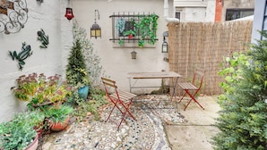 A small patio with a tiled floor, a wooden table, two red folding chairs, and potted plants. - Centrally Located Philadelphia Townhome w/ Patio! (Philadelphia)