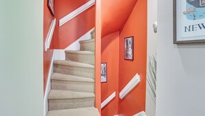 A staircase with beige carpet and white handrails, leading to a room with orange walls and a framed picture of a cityscape. - Centrally Located Philadelphia Townhome w/ Patio! (Philadelphia)