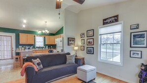 A living room with a sofa, ottoman, and a rug. There is a kitchen in the background with wooden cabinets and a refrigerator. - Hike Shenandoah! Family-friendly House w/ Deck (Shenandoah)