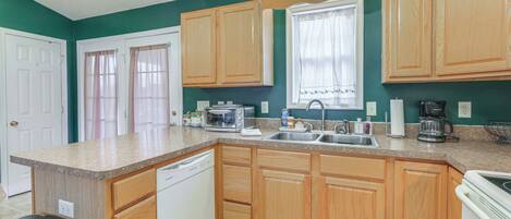 A kitchen with wooden cabinets, a dishwasher, a sink, and a window with curtains.