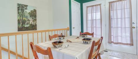 A dining area with a table set for four, wooden chairs, a painting on the wall, and a staircase with a railing.