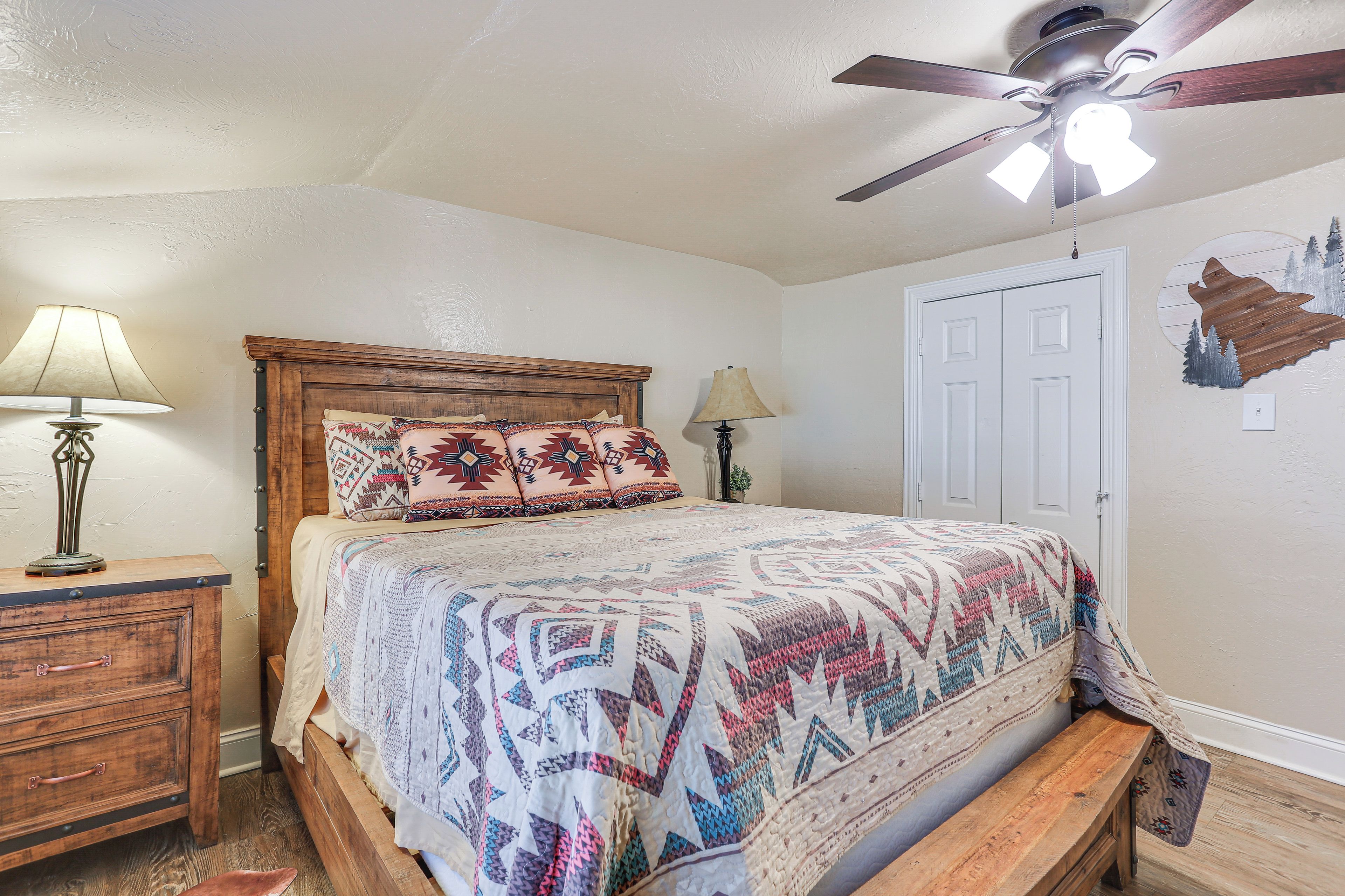 A bedroom with a wooden bed, two bedside lamps, a ceiling fan, and a door.