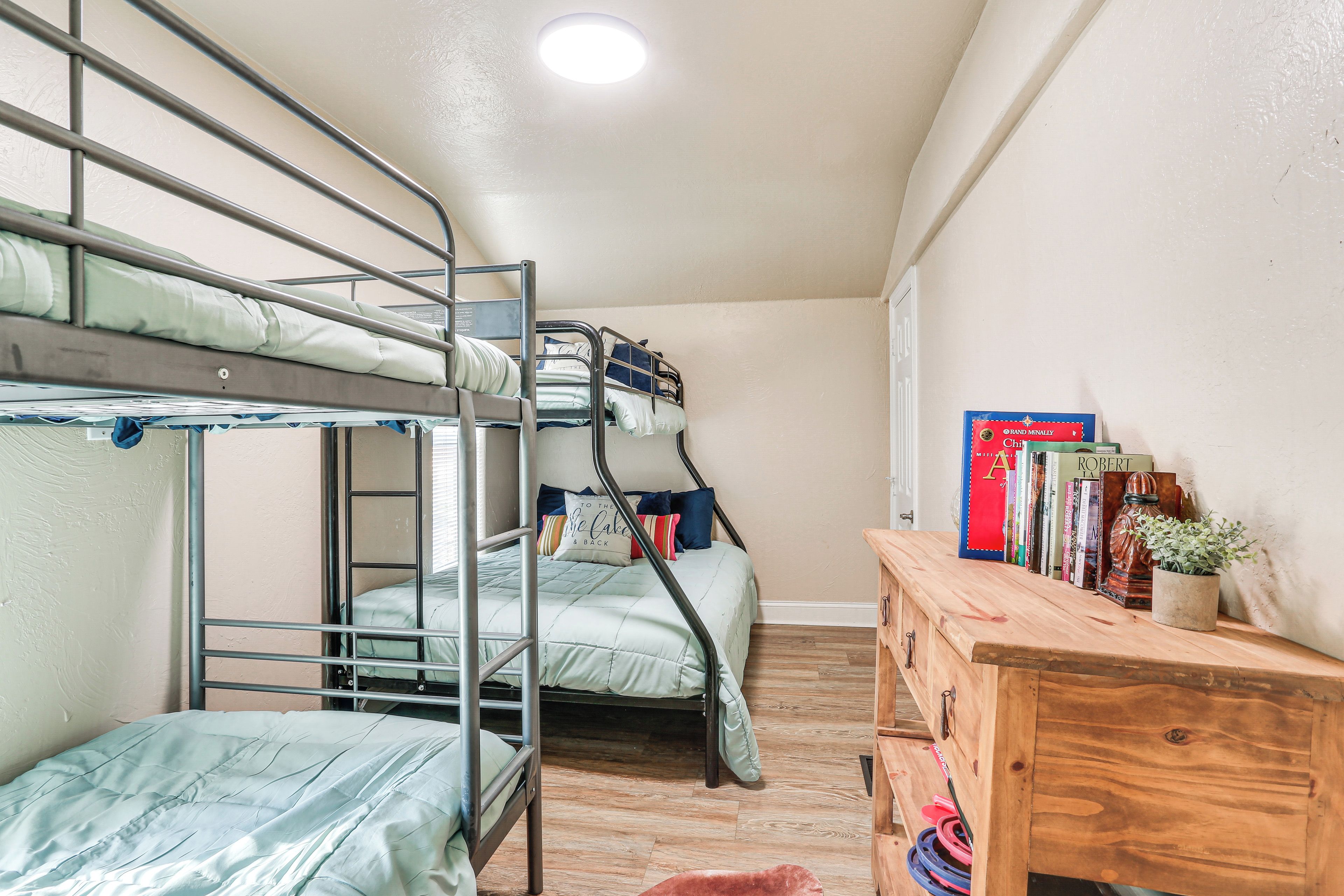 Een slaapkamer met een stapelbed, een houten dressoir en boeken.