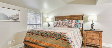 A bedroom with a wooden bed, two bedside tables with lamps, a window with blinds, and a ceiling fan.