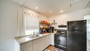 A kitchen with white cabinets, a black refrigerator, a stove, and a microwave. - Cozy Canyon Lake Cottage Rental w/ Private Hot Tub (Canyon Lake)