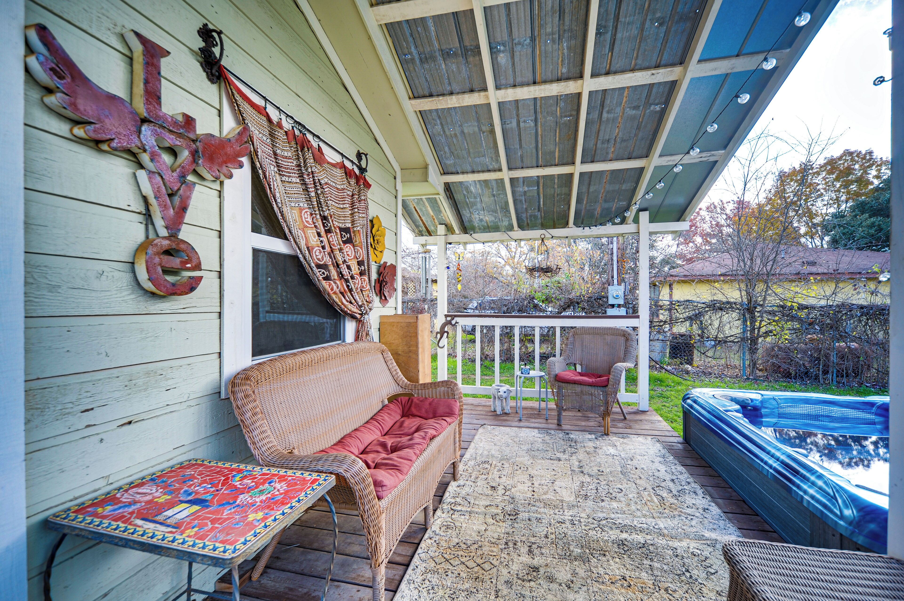 A covered porch with a wicker sofa, a small table, and a hot tub.