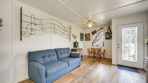 A room with a blue sofa, wooden flooring, a ceiling fan, a dining area with a table and chairs, and a door with a window. - Cozy Canyon Lake Cottage Rental w/ Private Hot Tub (Canyon Lake)