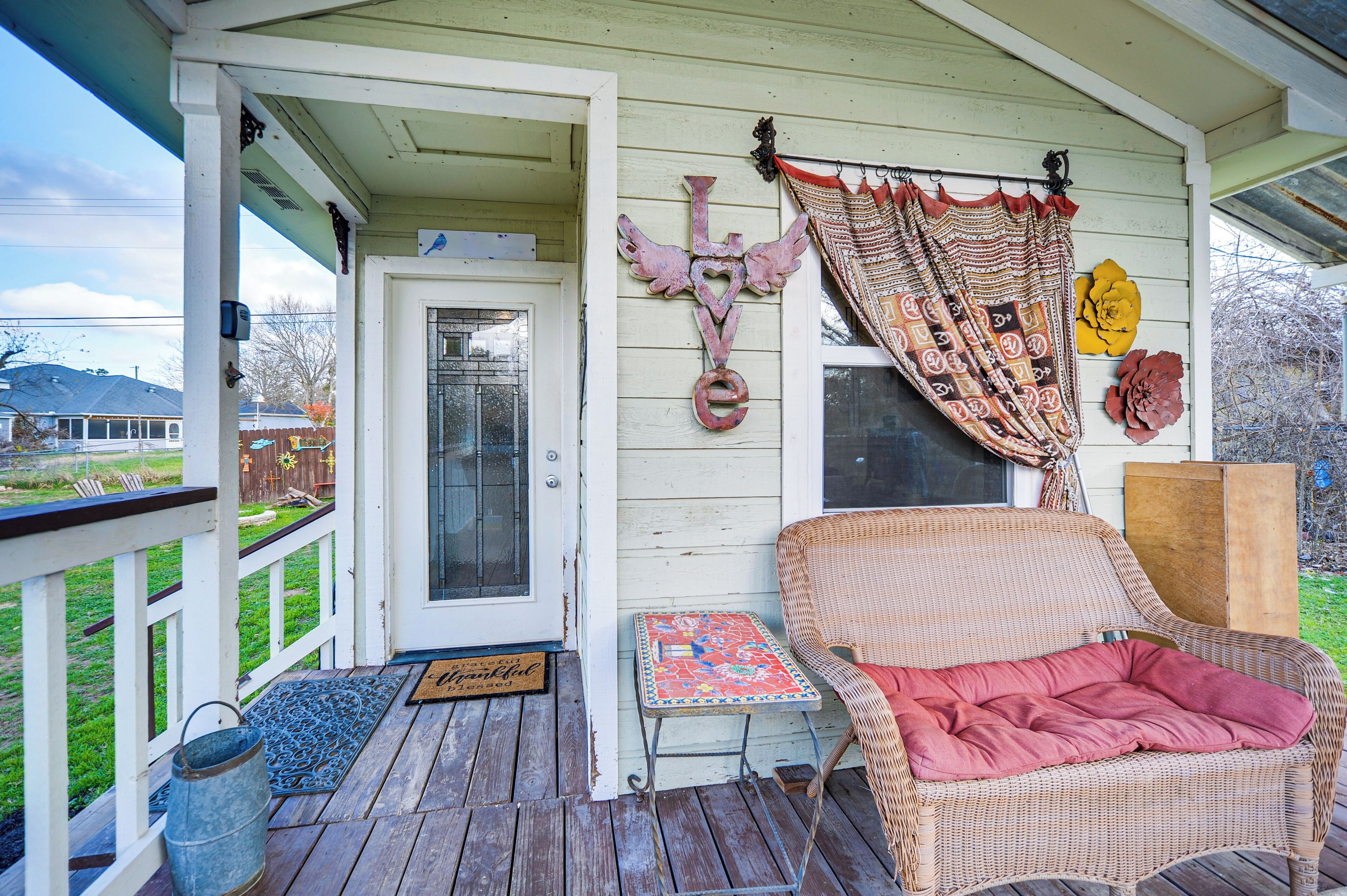 A porch with a wicker chair, a small table, and a decorative wall piece.