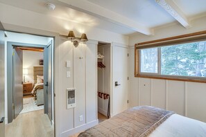 Un dormitorio con cama, ventana con vistas a árboles, armario y puerta que da a otra habitación.