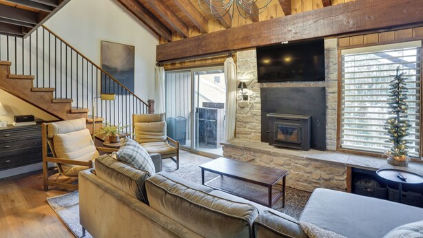 A spacious living room with a stone fireplace, a large TV mounted on the wall, and a cozy seating area with a sofa and chairs. - Mountain-view Condo in Brian Head w/ Private Sauna (Brian Head)
