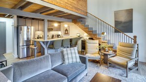 A spacious living area with a grey sofa, a wooden ceiling, a staircase, and a kitchen in the background. - Mountain-view Condo in Brian Head w/ Private Sauna (Brian Head)