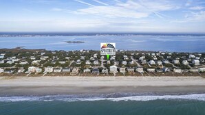 Vue aérienne d’un quartier résidentiel situé sur la côte, avec des maisons, une plage et un panneau indiquant les propriétés locatives de Spectrum.