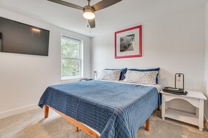 A bedroom with a bed, a nightstand, a ceiling fan, a window, and a framed picture on the wall.