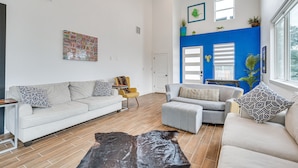 Un salon avec un canapé blanc, un fauteuil gris et un pouf, une table basse en bois et un mur d’accent bleu.