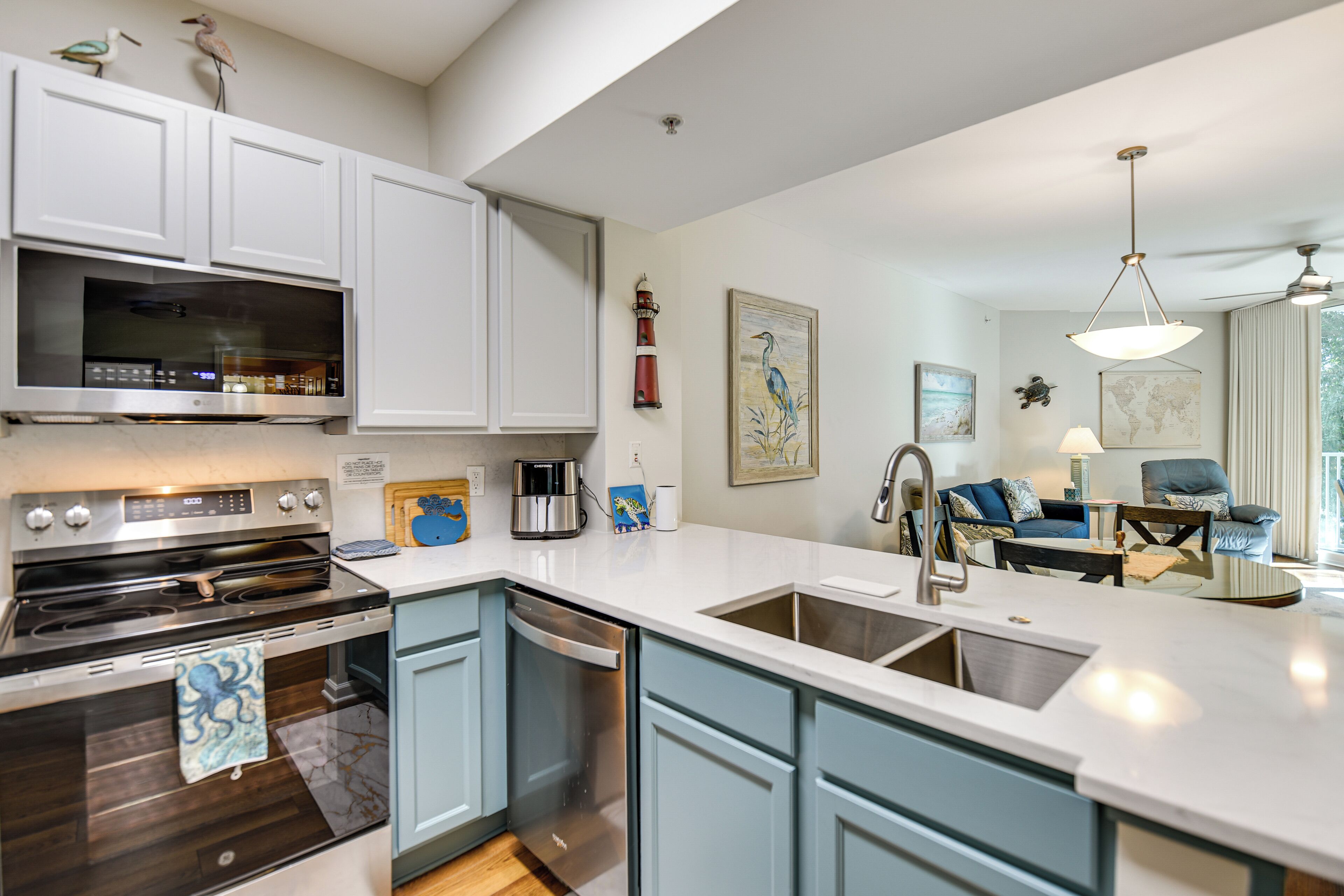 A modern kitchen with white cabinets, a built-in oven, and a dishwasher. There is a dining area with a blue sofa and a table.