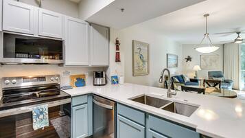 A modern kitchen with white cabinets, a built-in oven, and a dishwasher. There is a dining area with a blue sofa and a table.