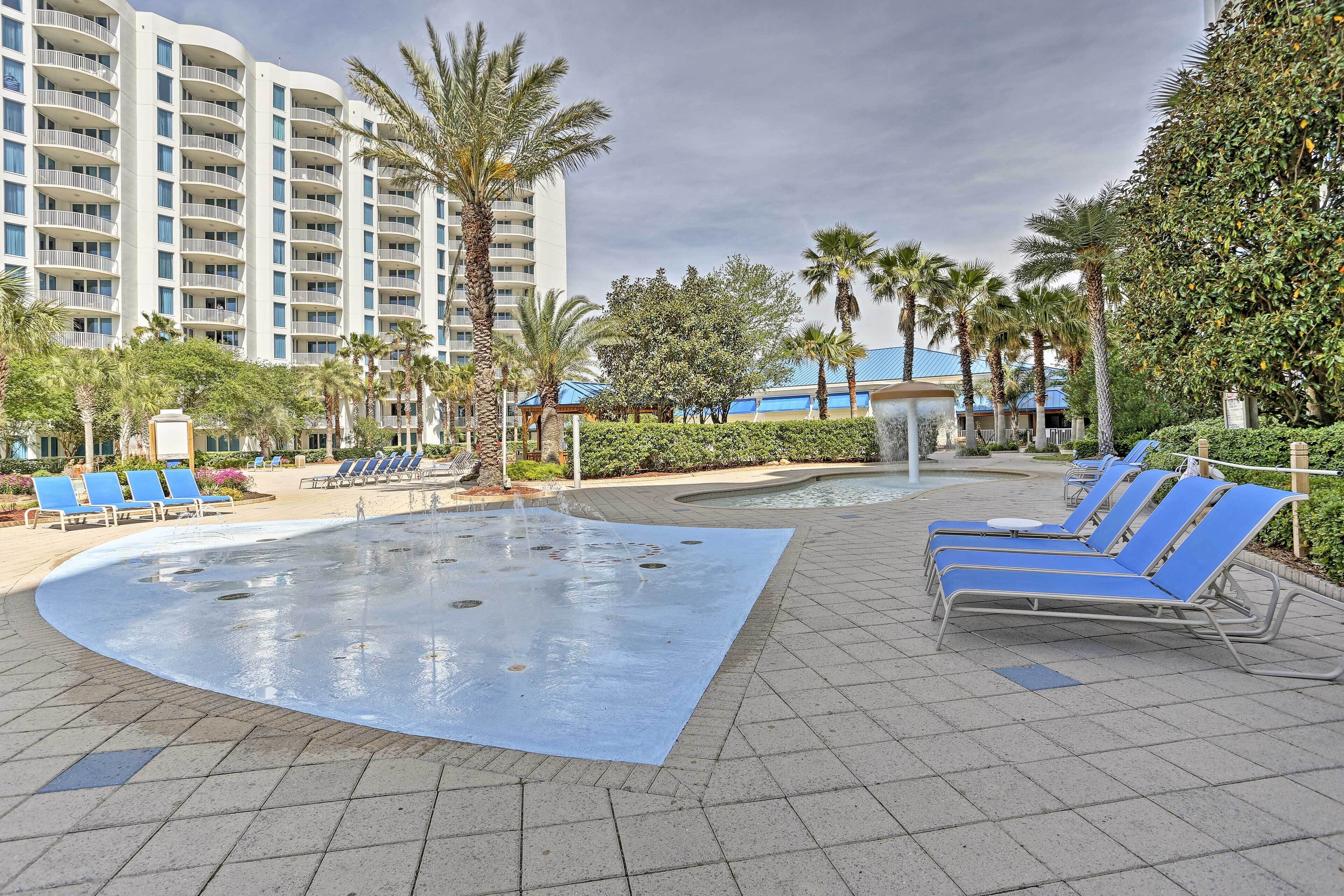 A pool area with blue lounge chairs, palm trees, and a large building in the background.