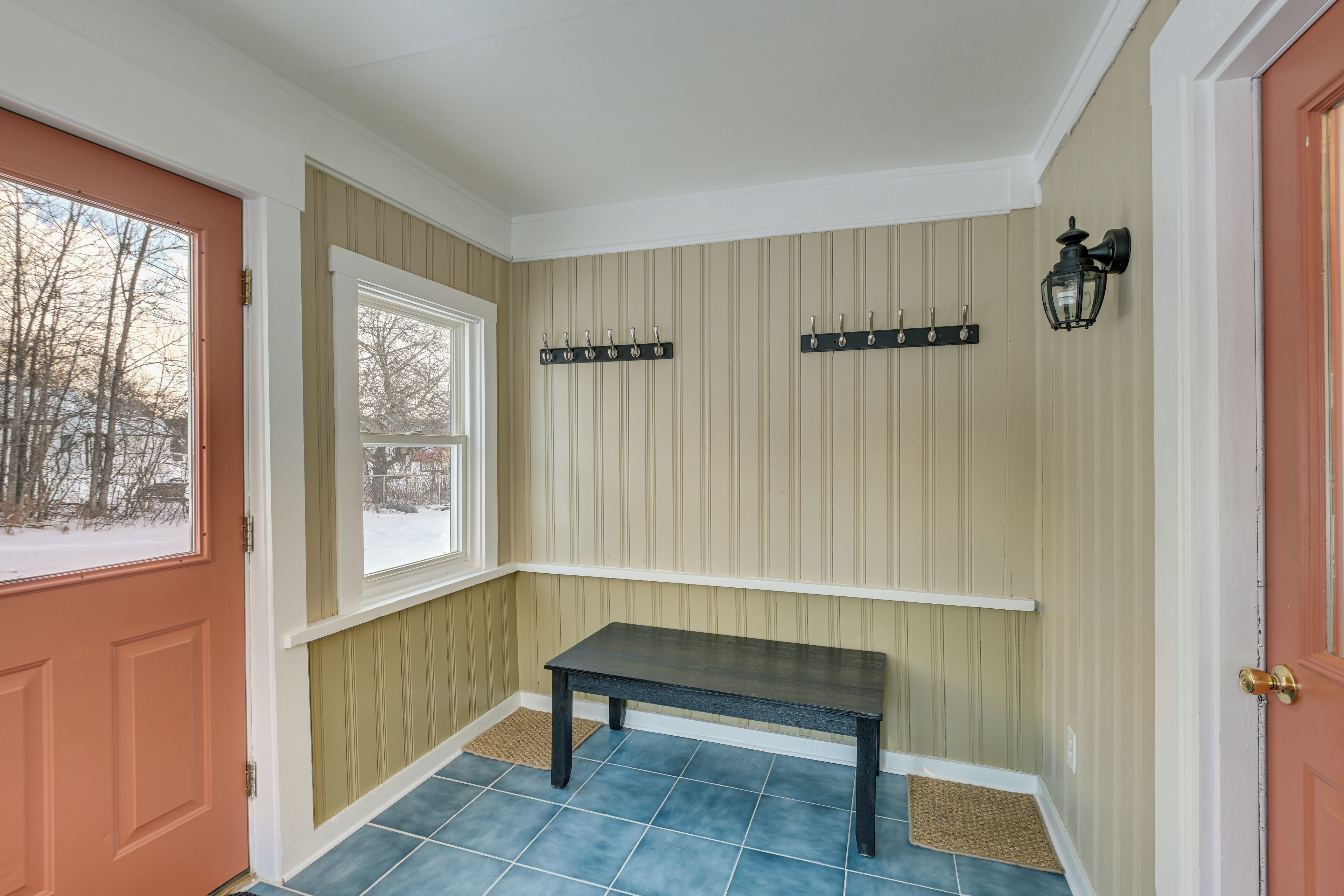A hallway with a bench, a coat rack, and a wall-mounted light fixture.