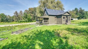 A small, single-story house with a porch and a sloped roof, surrounded by a grassy area and trees. - Maine Vacation Rental < 1 Mi to Portage Lake Beach (Portage)