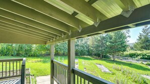 A wooden deck with a railing overlooking a grassy yard with trees and a fence. - Maine Vacation Rental < 1 Mi to Portage Lake Beach (Portage)