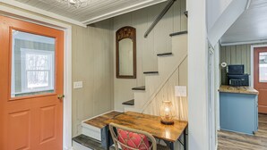 A staircase leading to a second floor, a wooden table with a chair, a mirror, and a kitchen area with appliances. - Maine Vacation Rental < 1 Mi to Portage Lake Beach (Portage)
