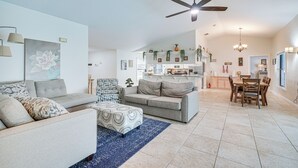 Un salon spacieux avec un canapé gris, un pouf à motifs et un coin repas comprenant une table et des chaises en bois.