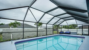 Une piscine couverte dotée d’une structure de toit aux lignes géométriques, entourée d’un mur bas et d’un petit espace aménagé pour s’asseoir.