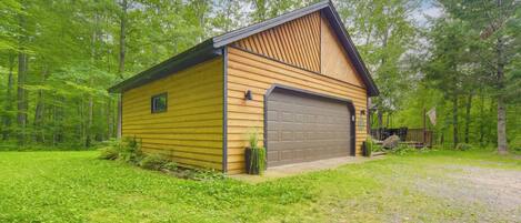 A single-story wooden cabin with a garage, surrounded by a forested area.