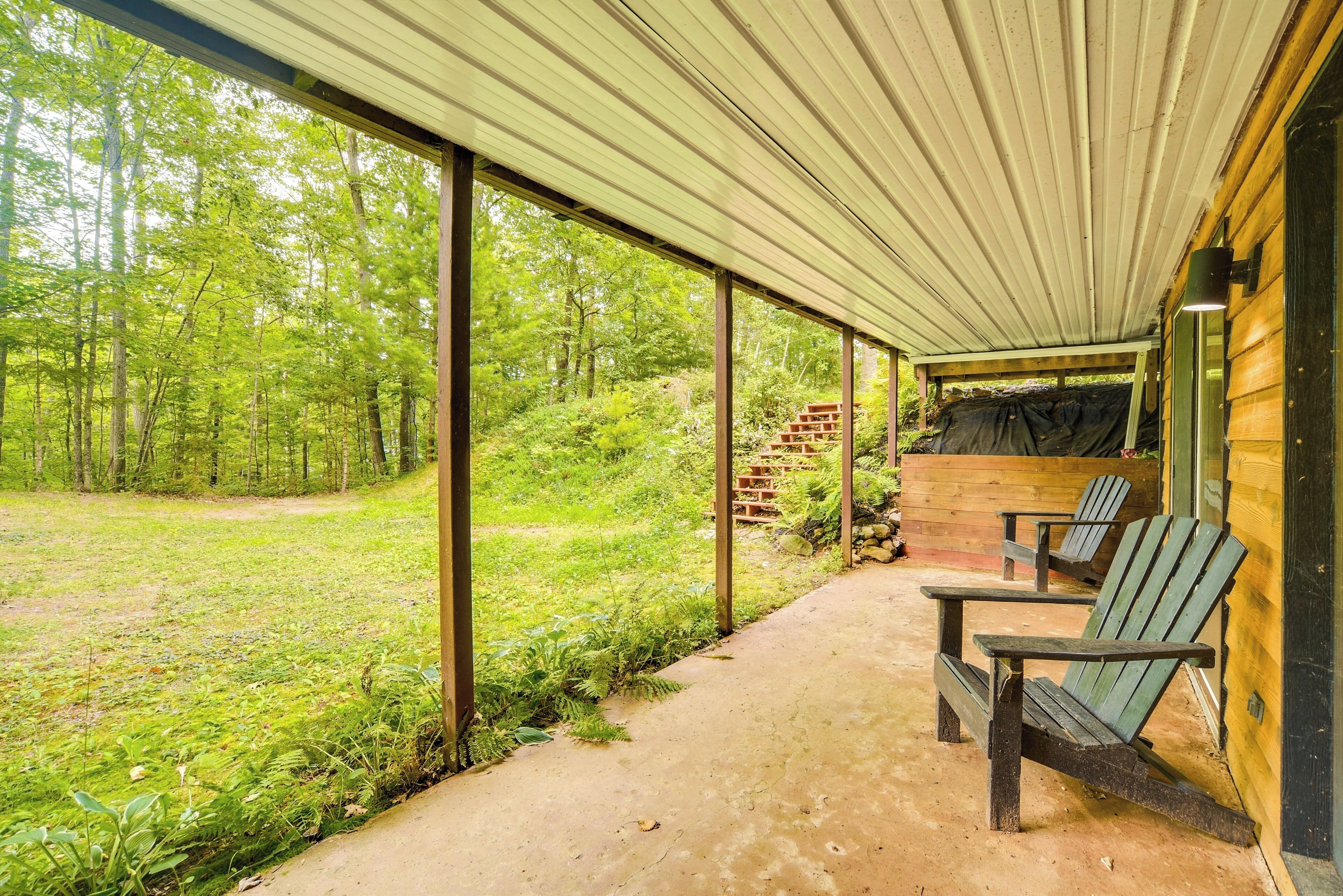 A covered porch with two Adirondack chairs, a brick wall, and a view of a forested area.