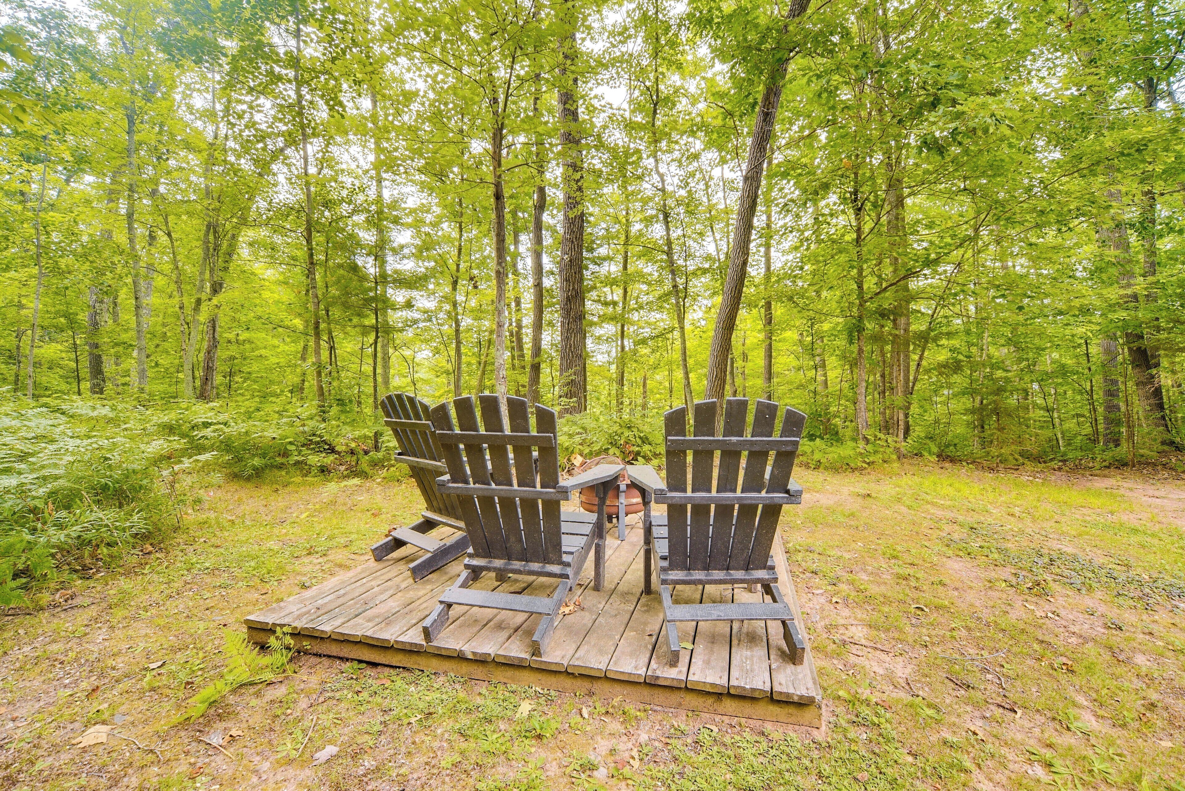 Twee Adirondack stoelen op een houten terras in een bebost gebied.