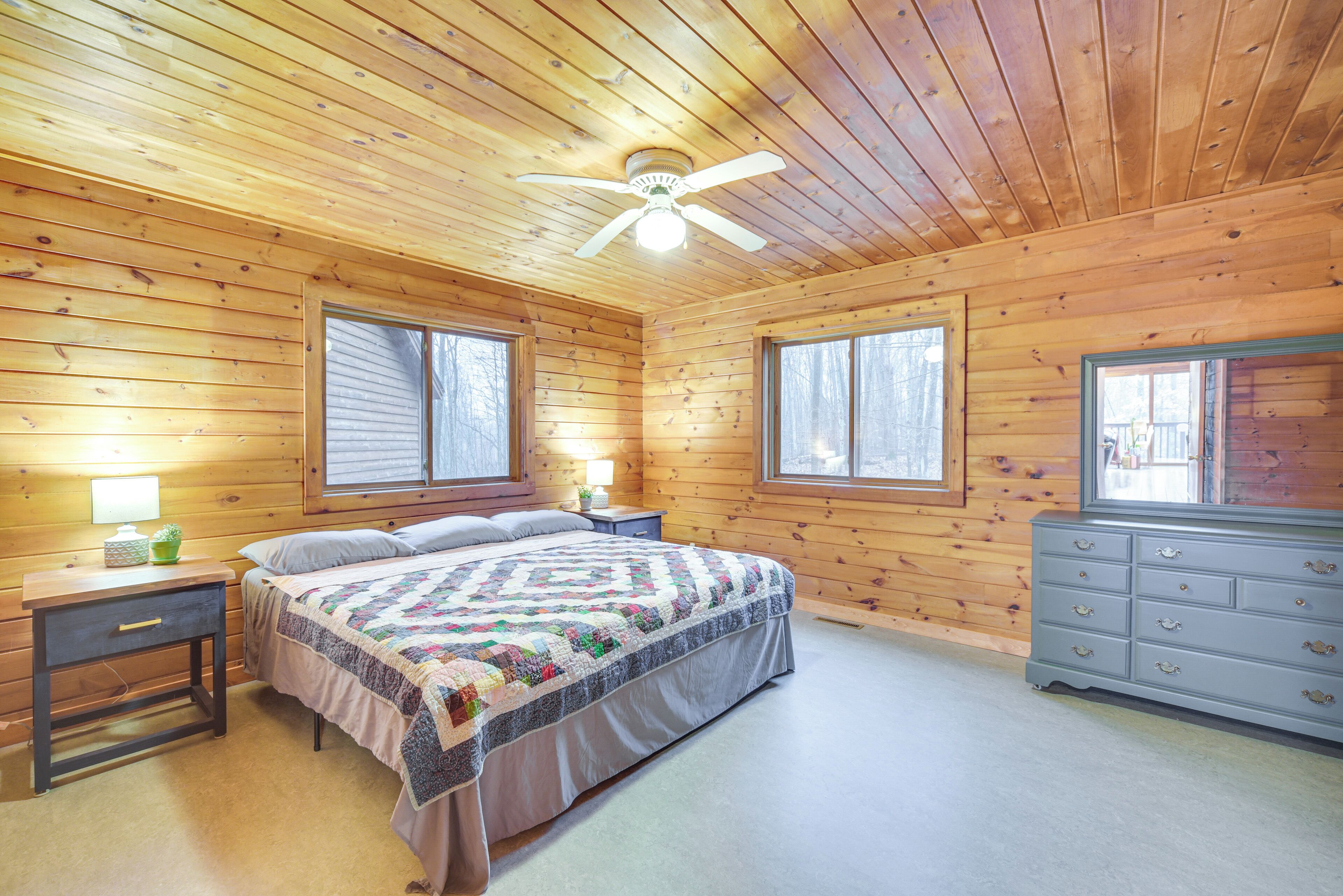 Un dormitorio de cabaña de madera con cama, cómoda, mesitas de noche y ventilador de techo.