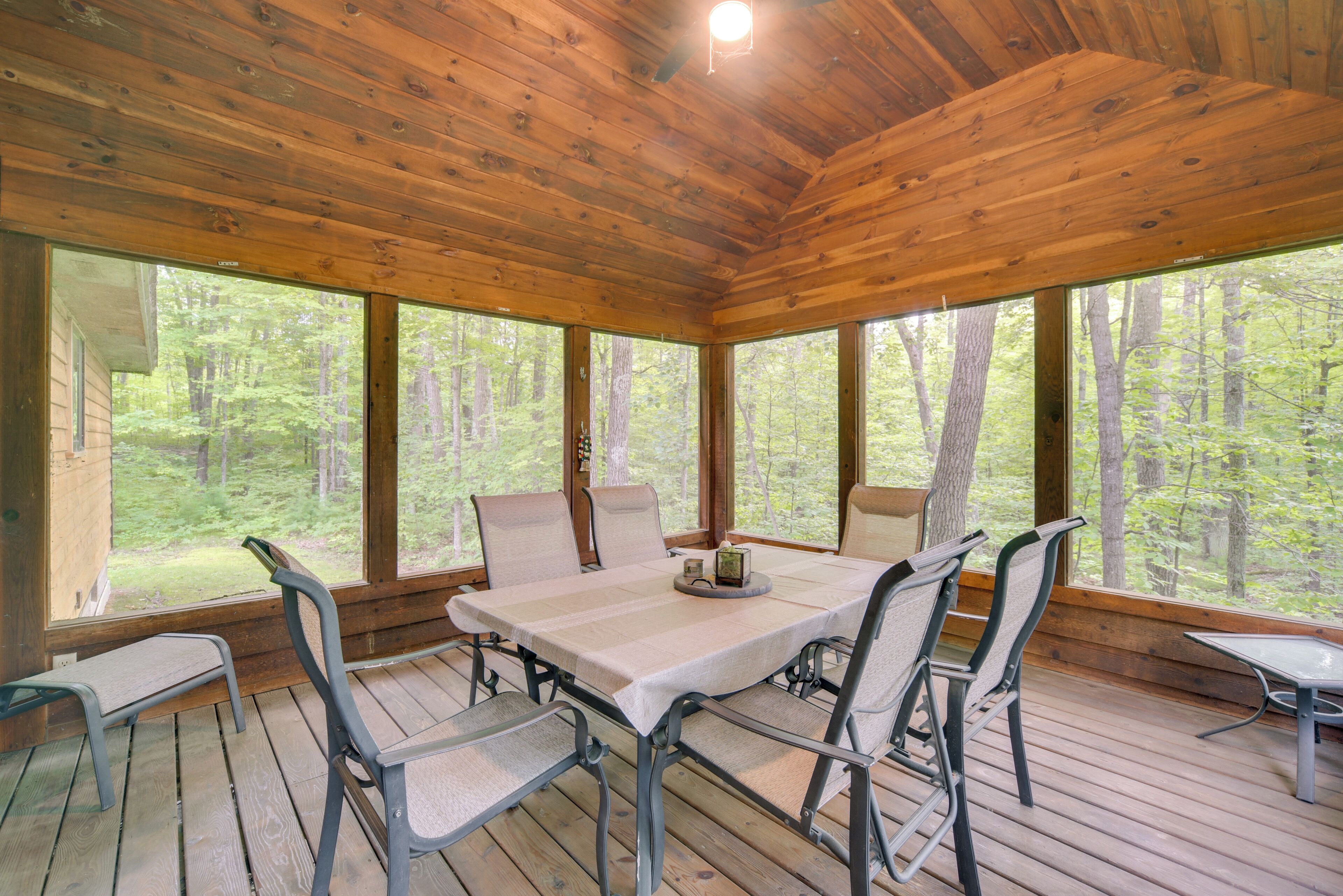 A wooden deck with a table and chairs, large windows, and a view of the forest.