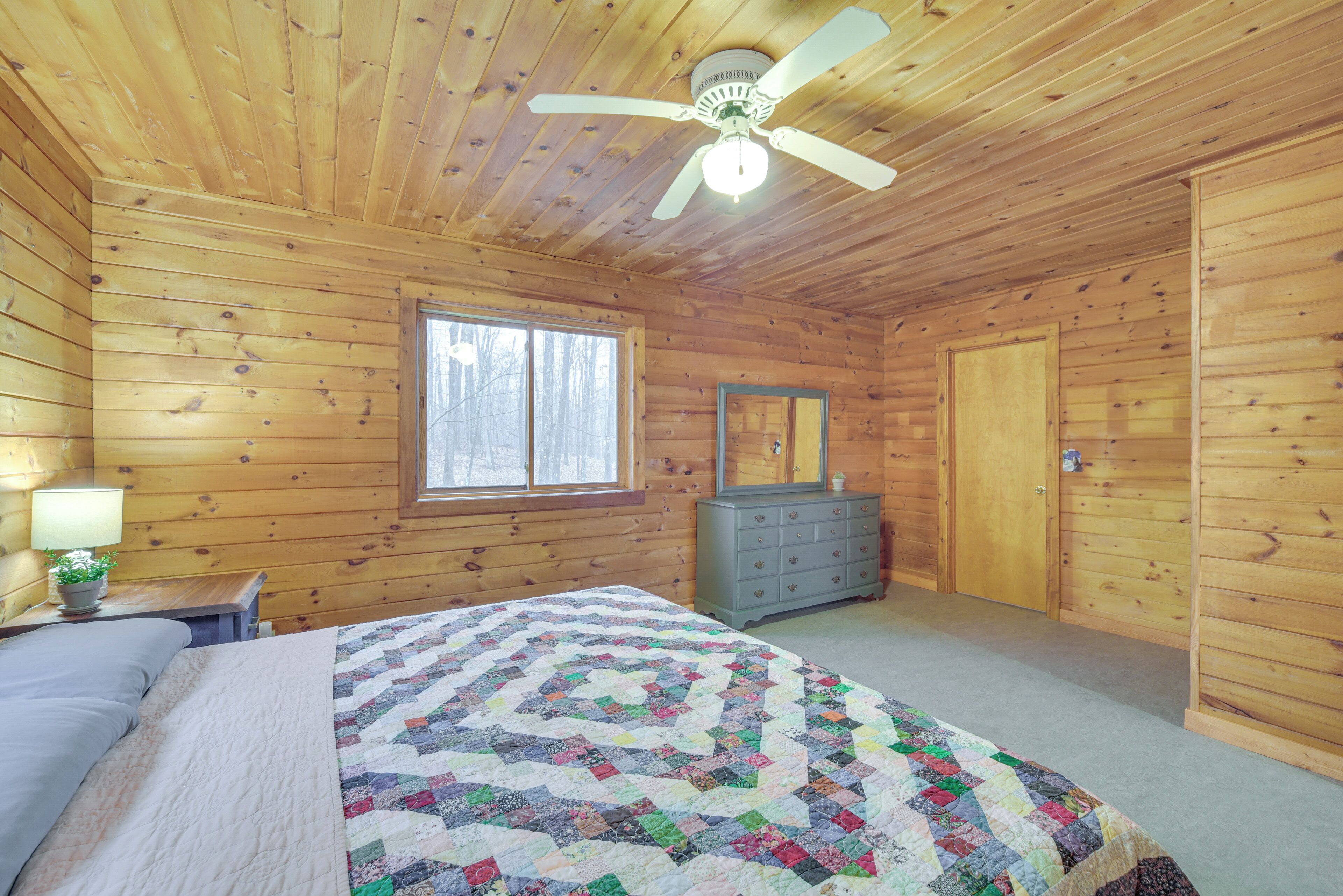 A wooden cabin bedroom with a bed, dresser, and a ceiling fan.