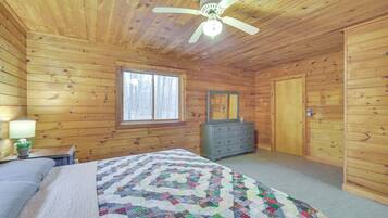 A wooden cabin bedroom with a bed, dresser, and a ceiling fan.