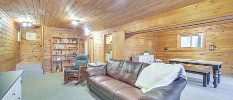 Un interior acogedor de cabaña con un sofá de cuero, estanterías de madera, una mesa de comedor y una silla.