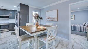 A modern kitchen with a wooden dining table, white chairs, and a large window. - Game Room + Screened Lanai: Pine Island Getaway! (Saint James City)