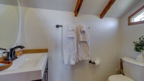 Une salle de bain avec un lavabo blanc, un plan de toilette en bois et des toilettes. Des serviettes sont suspendues sur un porte-serviettes et une plante est posée sur le réservoir des toilettes.