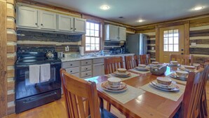 Une cuisine rustique avec des meubles de rangement en bois, un poêle et une table à manger dressée pour six personnes, avec des sets de table et des bols.