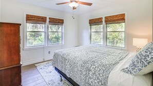 Une chambre à coucher avec un lit, un ventilateur de plafond et des fenêtres équipées de stores.