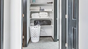 Un couloir étroit avec un panier à linge blanc et des serviettes soigneusement pliées, rangées sur des étagères.