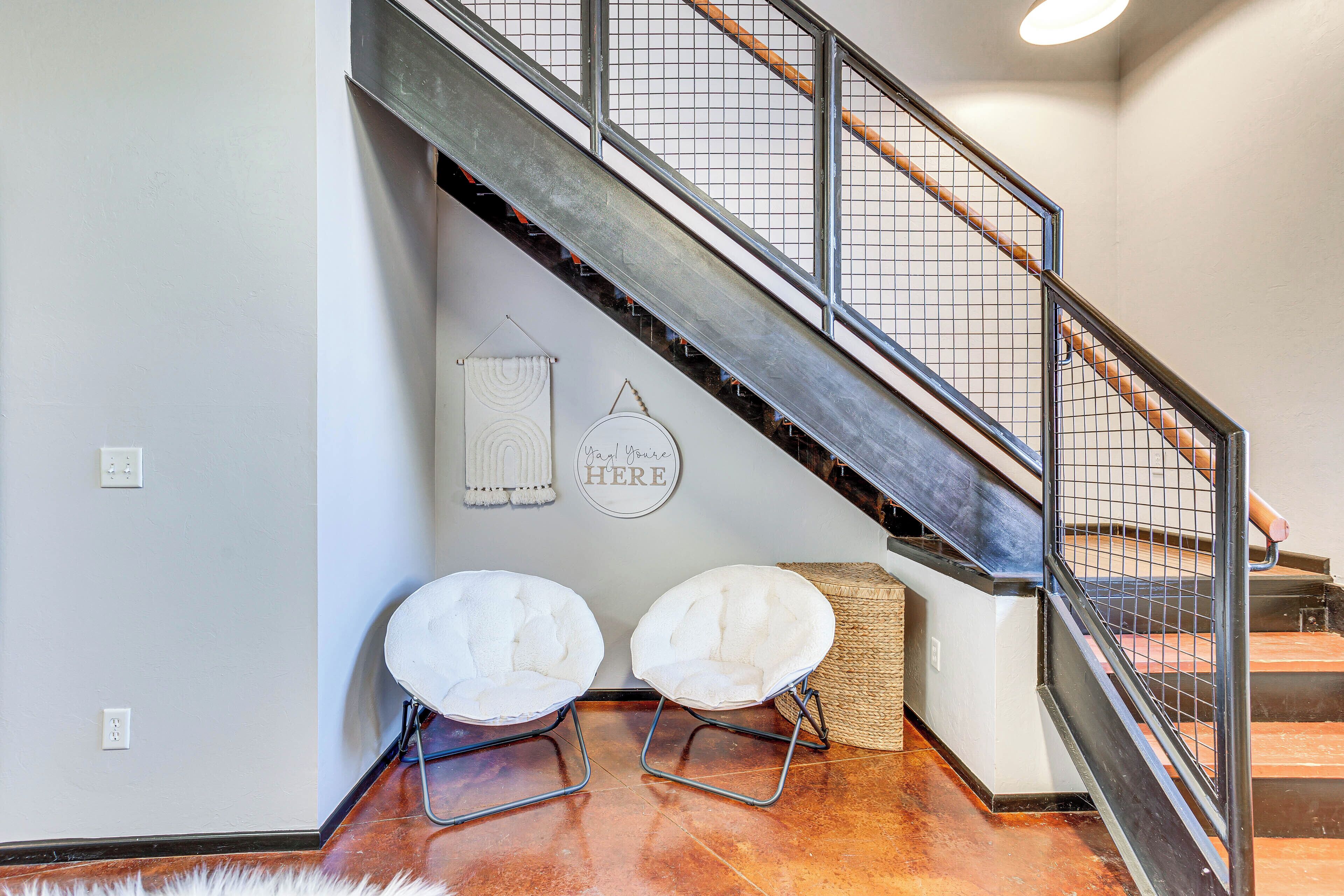 A staircase with metal railings, a white wall with a circular sign, and two white chairs with metal frames.