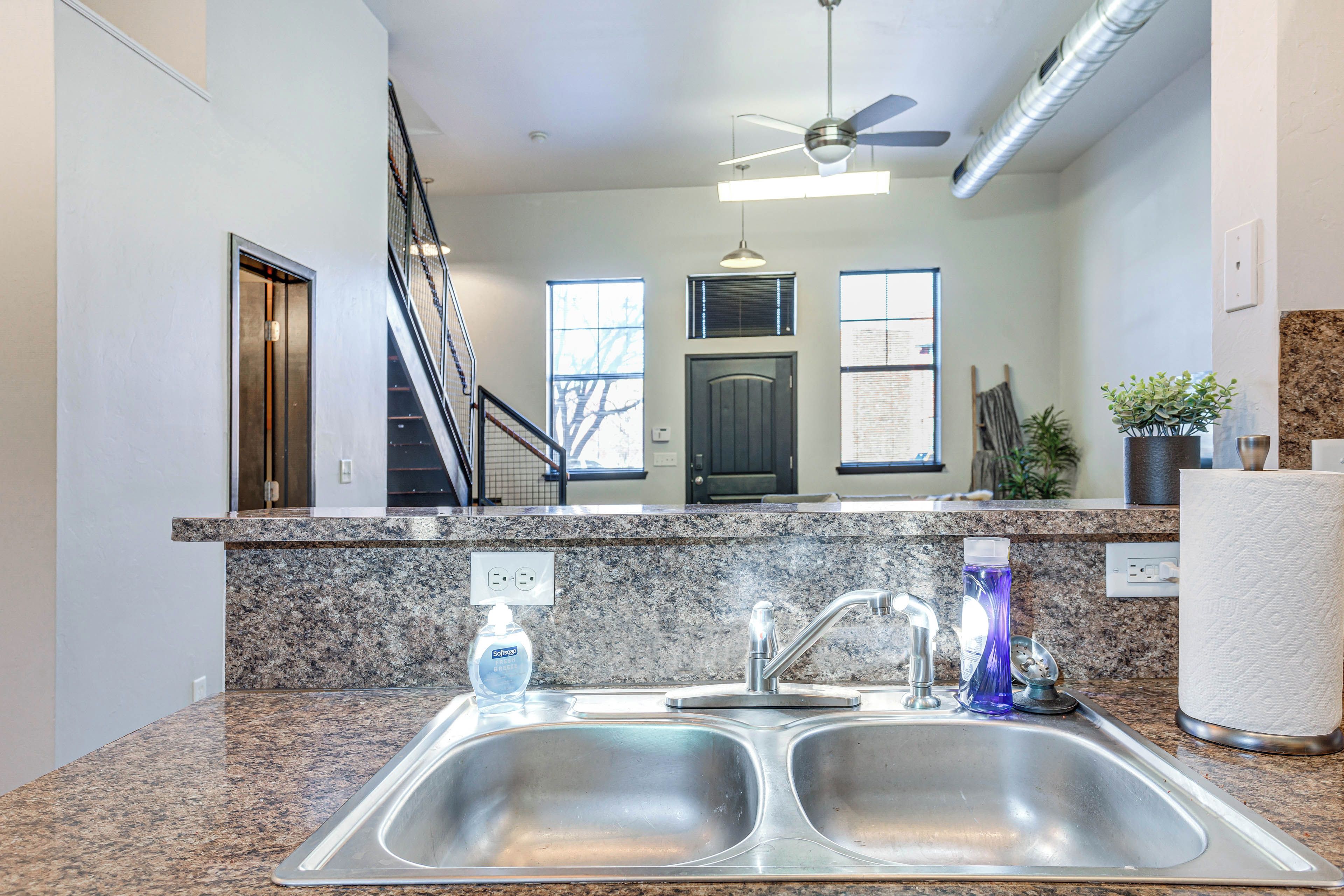 A kitchen with granite countertops, a double sink, a ceiling fan, and a staircase leading to another level.