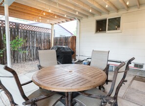 Eine überdachte Terrasse mit einem runden Holztisch und vier Stühlen, einem Grill und einem Holzzaun.