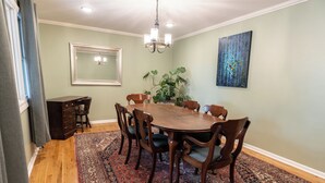 Une salle à manger avec une table et des chaises en bois, un lustre, un grand miroir et un tableau accroché au mur.