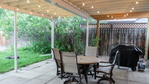 Une terrasse couverte avec une table et des chaises, un barbecue et une guirlande lumineuse.