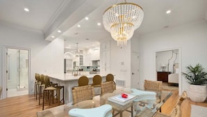 A modern living room with a glass dining table, wicker chairs, and a chandelier.