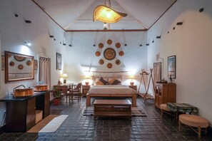 A cozy bedroom with a large bed, a wooden bench, a small table, and a hanging light fixture. - Samsara Apartments by Babermahal Revisited (Kathmandu)